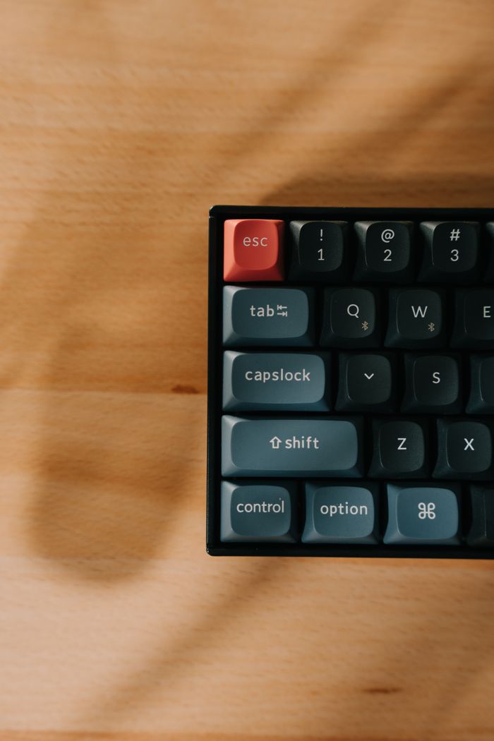 Services Top view of a mechanical keyboard with a red escape key on a wooden desk.
