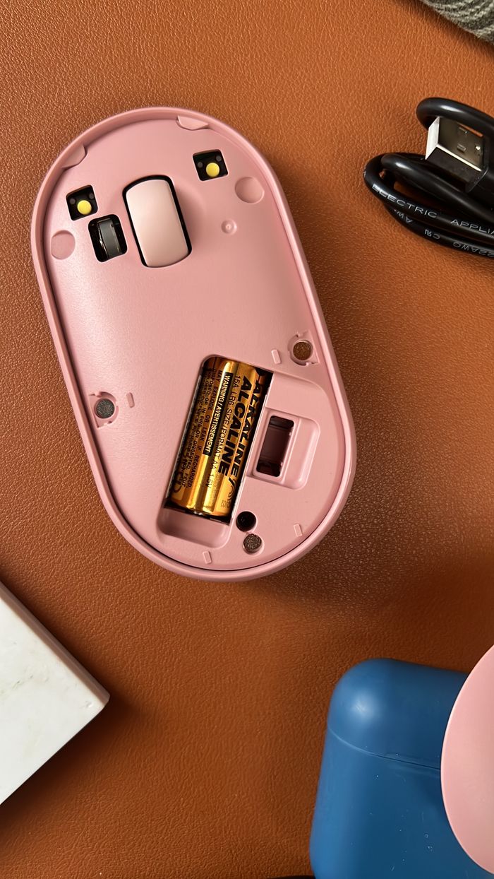 Services Close-up of an open pink wireless mouse revealing batteries on a desk.